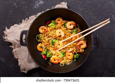 Stir fried noodles with shrimps and vegetables in a wok on dark table, top view