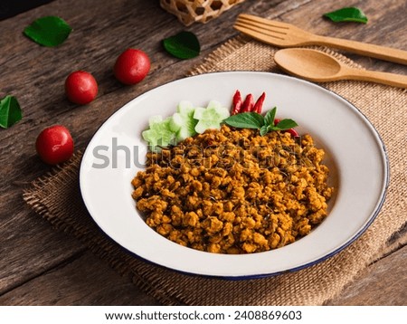 Stir fried pork with yellow curry paste in white plate on wooden table background. Traditional Thai southern food
