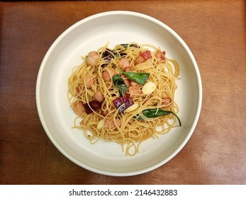 Stir fried spaghetti with dried chili and crispy bacon in white plate on wooden background.