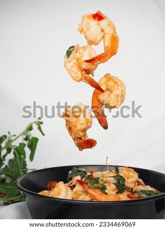 Stir fried Thai basil with shrimp falling into pan on white fabric background. Thai food
