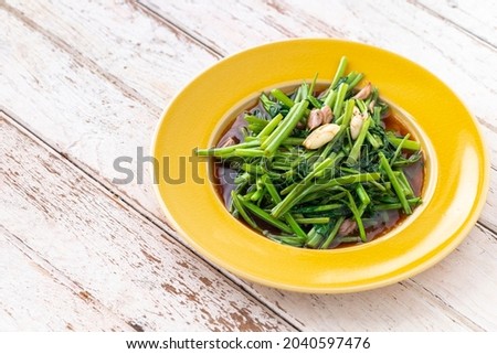 stir fried water spinach with garlic in yellow ceramic plate on white old wood texture background with copy space for text, light and airy food photography, morning glory