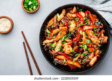 Stir fry with chicken, red paprika, mushrooms and chives in frying pan. Asian cuisine dish. Gray kitchen table background, top view, copy space
