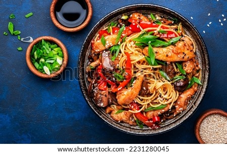Stir fry noodles with chicken, red paprika, mushrooms, chives and sesame seeds in bowl. Asian cuisine dish. Blue table background, top view