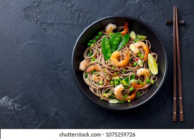 Stir fry noodles with vegetables and shrimps in black bowl. Slate background. Top view. Copy space. - Shutterstock ID 1075259726
