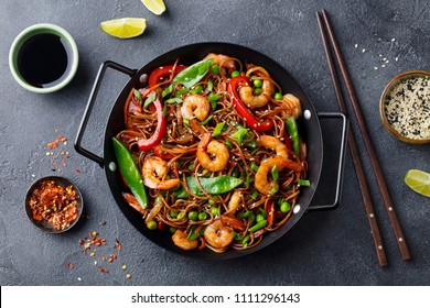 Stir fry noodles with vegetables and shrimps in black iron pan. Slate background. Top view.
