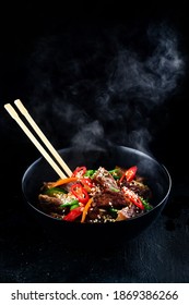 Stir fry soba noodles with beef and vegetables in wok on dark background, Asian udon noodles with beef WOK in black bowl on Slate background. Copy space