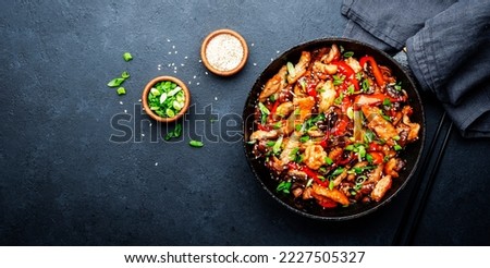 Stir fry with turkey fillet, paprika, mushrooms, green chives and sesame seeds in frying pan. Asian cuisine dish. Black stone kitchen table background, top view
