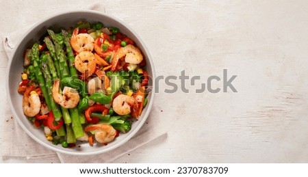 Stir fry vegetables and shrimps in a white plate on a light background. Top view.