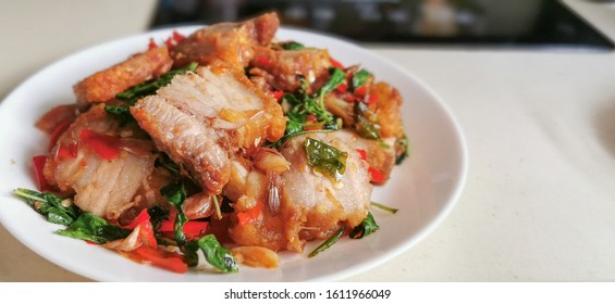 Stir-Fried Crispy Pork and Basil in white plate on table.