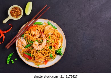 Stir-fried spaghetti or stir-fry noodles with vegetables and shrimp on the plate. dark background, top view