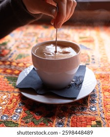 Stirring with a spoonful of coffee mug, adding sugar to Masala chai an Indian restaurant, spiced milk tea, traditional cardamom hot drink with spices, muted shades, blurred background