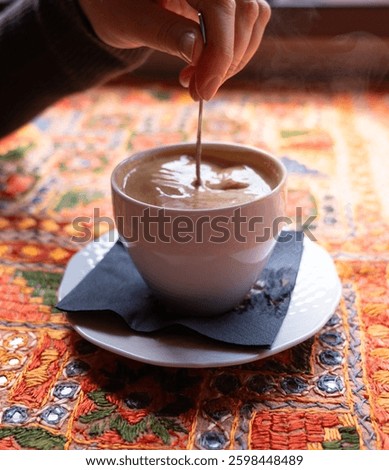 Stirring with a spoonful of coffee mug, adding sugar to Masala chai an Indian restaurant, spiced milk tea, traditional cardamom hot drink with spices, muted shades, blurred background