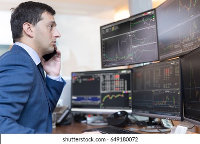 Stock Broker Trading Online While Accepting Orders By Phone. Trader's Office With Multiple Computer Screens Full Of Index Charts And Data Analyses.