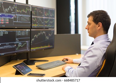 Stock Broker Trading Online While Accepting Orders By Phone. Trader's Office With Multiple Computer Screens Full Of Index Charts And Data Analyses.