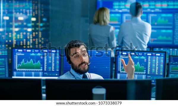Stock Exchange Trader\
Makes a Deal with Big Client Over the Headset. He Works with Other\
Brokers and is Surround By Computers with Graphs and Ticker Numbers\
on Screens.