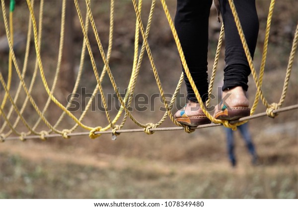 Stock image of Female foot is walking\
on a suspension  rope bridge. She is doing outdoor adventure\
activities like rope balancing act with family on\
vacation.