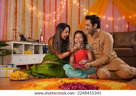 Stock image of a happy family - mother loving her daughter. Making rangoli and enjoying Diwali. Indian mother and father loving their daughter and sitting together to make rangoli - home decoration...