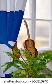 Stock Image Of Two Classical Guitars On The Windowsill Near The Window With Blue And White Curtains Behind Green Fern