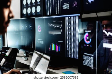 Stock market analysts monitoring real-time data, charts, and graphs on computer screens in a dark room. Financial investment and technology concept