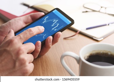 Stock market charts on smartphone screen.Closeup of male hands holding smartphone. Checking financial market.
