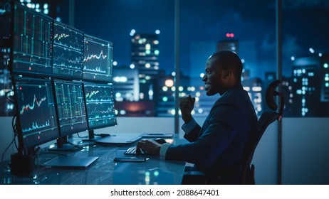 Stock Market Day Trader Working on Computer with Multi-Monitor Workstation with Real-Time Investmentment Charts. Successful African American Businessman Punches Air for Winning a Trade.