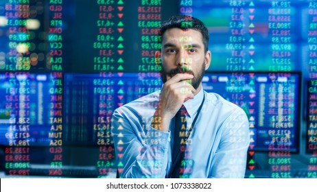 Stock Market Top Trader Looks at Projected Ticker Numbers and Graphs Running, Analysing Data to Make Best Sell. Behind Him Room Full of Screens and Statistics.