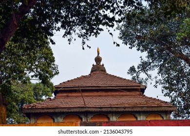 stock photo of ancient hindu temple peak, pyramid shape roof top covered with clay made tiles and peak made up by bronze metal. Temple surrounded by green trees, blue sky on background at Kolhapur.
