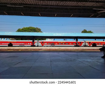 Stock photo of empty railway station or platform under gray color shelter, steel and wooden benches, drinking water taps for passenger at platform. red color train passes railway platform in India.