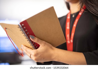 Stock photo of hands of a girl with an open notebook of recycled material and red details. Office work.