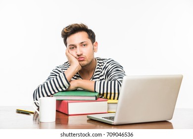 Stock Photo Of Handsome Indian Boy / Male College Student Studying On Study Table With Pile Of Books, Laptop Computer And Coffee Mug. Smiling Or Thinking/worried/showing Thumbs Up / With Smartphone
