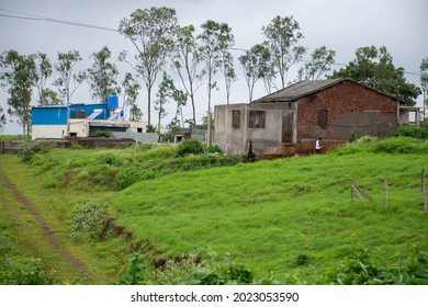 Stock photo of a house constructed with red bricks in between green grass and trees, blue color shelter, water tank and solar panel installed beside the house in monsoon sean at Indian village