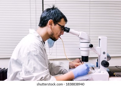 Stock photo of male scientist wearing face mask using a microscopy in his lab.