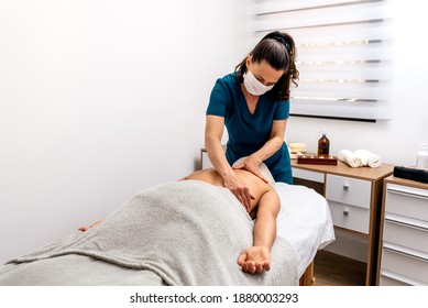 Stock photo of physiotherapist wearing face mask giving massage to patient lying in stretcher. - Powered by Shutterstock