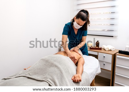 Stock photo of physiotherapist wearing face mask giving massage to patient lying in stretcher.