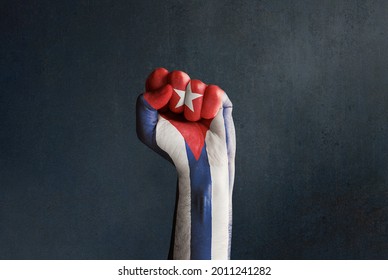 Stock Photo Of A Raised Fist With Cuban Flag On A Dark Background And Copy Space. SOS Cuba, Free Cuba, Protests In Cuba Against The Government Fighting For Freedom And Democracy