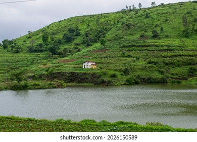 Stock photo of a scenic view of a slops of mountain range covered with green cultivation land and white painted house located in the middle of the mountain range.Water lake flowing around the mountain - Shutterstock ID 2026150589