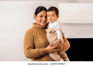 Foto de archivo de una mujer sonriente sosteniendo a su bebé y mirando a la cámara.