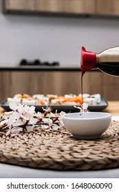 Stock Photo With Soy Sauce Falling In White Bowl Surrounded By Pieces Of Sushi And Sakura Blossom In A Modern Kitchen.