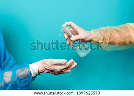 Stock photo of unrecognized healthcare worker wearing protective clothing applying hand sanitizer against blue background.