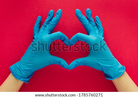 Stock photo of a woman's hands with blue gloves forming a heart with her fingers on a red background