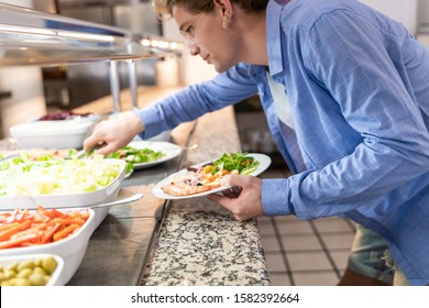 Stock photo of a young man bent over taking salad from a self-service. Lifestyle