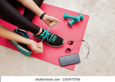 Stock photo of a young woman tying her shoelaces at home in the living room for fitness - Powered by Shutterstock