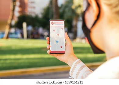 Stock photo of a young woman using a Coronavirus tracking app in her phone while is on the street