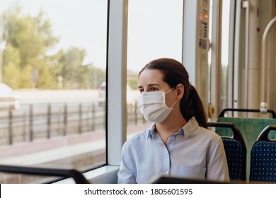 Stock photo of a young woman wearing a face mask traveling by tram. She is looking out the window. New normal concept