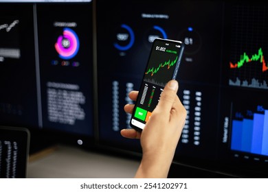 Stock trader is analyzing real-time charts on mobile phone and multiple computer screens showing financial data. Stock market analysis. Financial investment and technology concept - Powered by Shutterstock