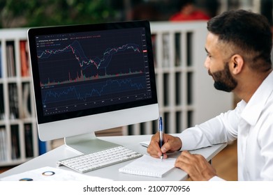 Stock Trading. Focused Successful Indian Trader Expert, Stock Broker, Using Computer In His Modern Office, Analyzing Cryptocurrency Market, Taking Notes, Planning Stock Strategy