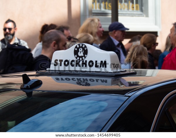 Stockholm, Sweden - 18 July\
2019 urban black taxi in the center of the Trangsund street, around\
different people. Taxi light box on black car in  Stockholm\
\
\
\
\
