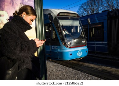 Stockholm, Sweden Feb 18, 2022 A young woman on phone waiting at a tram stop in Liljeholmen.