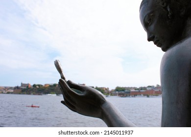 Stockholm, Sweden - June 26, 2019: Statue Of Woman Holding A Flower On The Stockholm City Hall Seafront With A View To Riddarfjärden