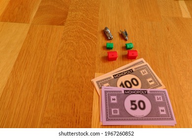 Stockholm, Sweden. May 02, 2021. Monopoly Items Against A Wooden Background. Classical Board Game.  Area With Copy Space. Red Hotel, Green House, Money And Metal Car.